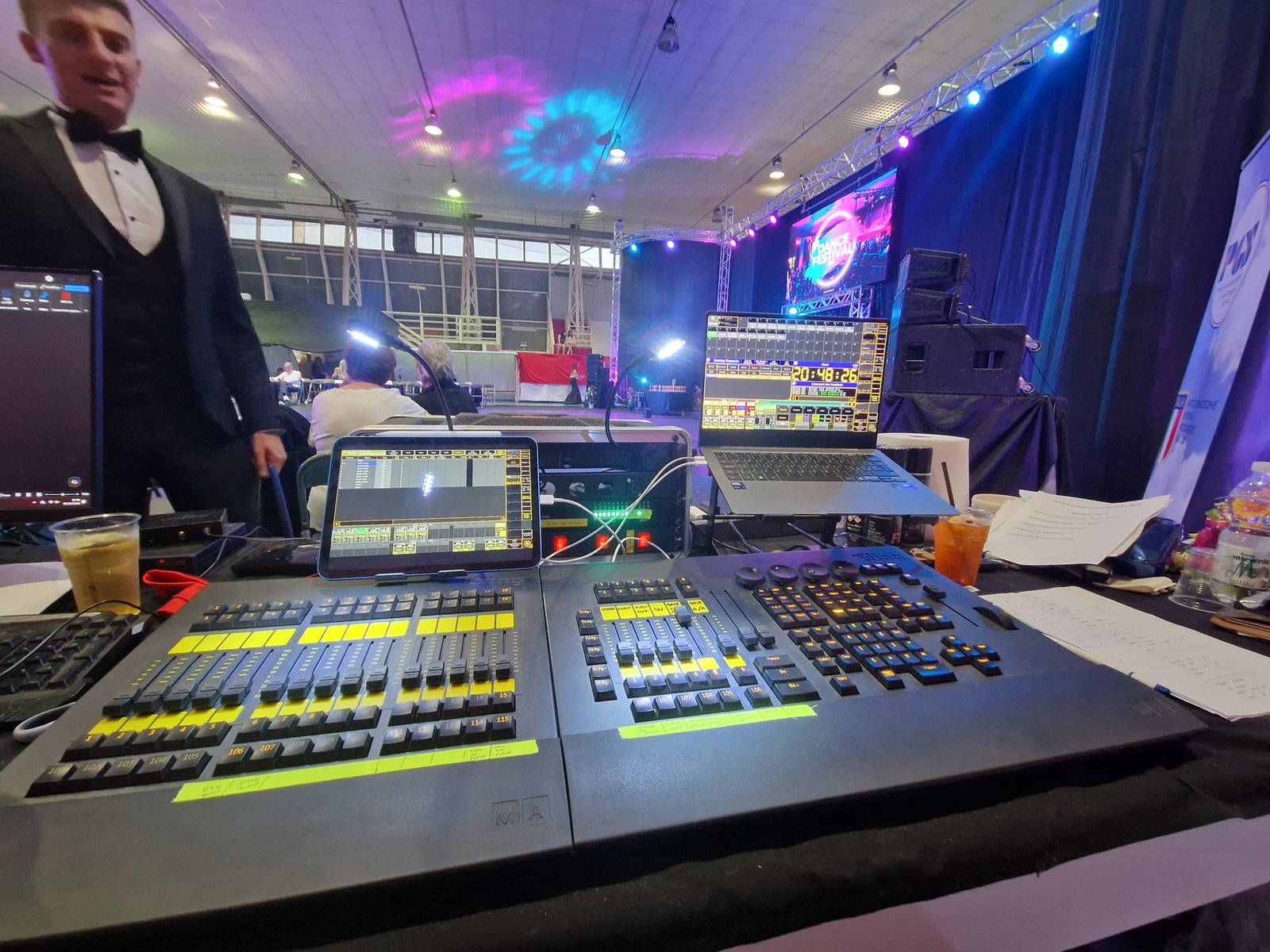 Console luci e computer nella postazione tecnica di un evento con palco e LED wall